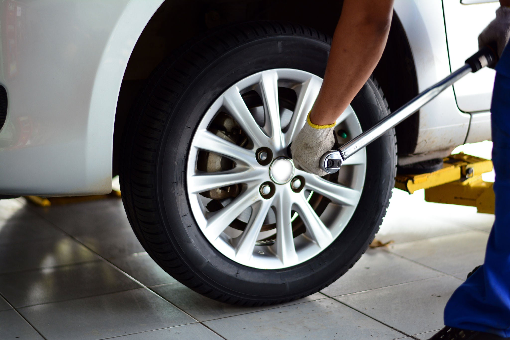 a mechanic in blue uniform  with white glove holding a pound wrench tighten the bolts of the wheel